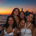 Four women posing together at sunset near water with city skyline in the background